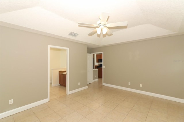 tiled empty room with ceiling fan and a raised ceiling