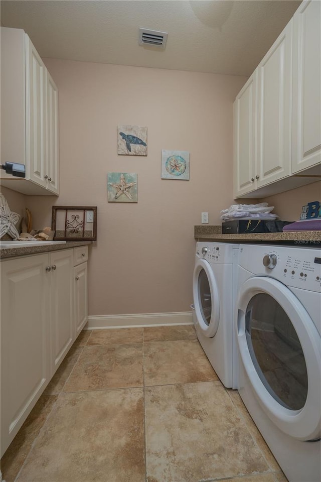 clothes washing area with washing machine and dryer, cabinets, and light tile floors