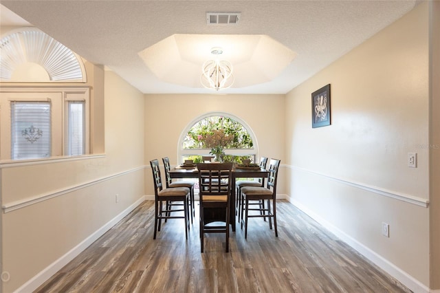 dining area featuring a textured ceiling, a tray ceiling, dark wood-type flooring, and a chandelier