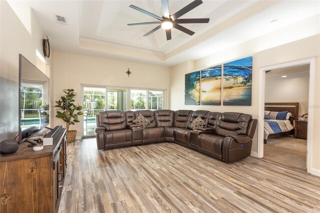 living room with ceiling fan, a raised ceiling, crown molding, and light hardwood / wood-style flooring