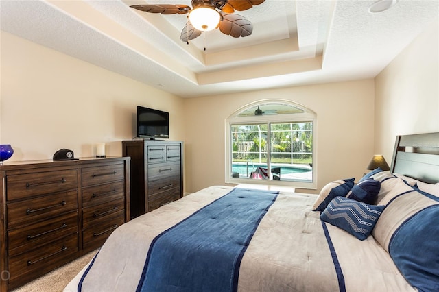 bedroom featuring a raised ceiling, access to exterior, a textured ceiling, ceiling fan, and light carpet