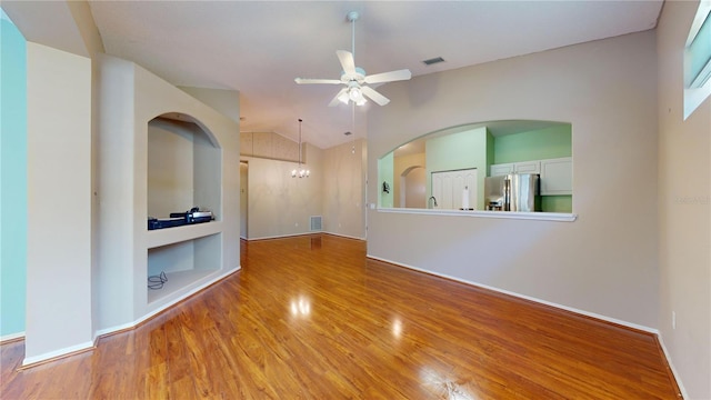 empty room with hardwood / wood-style floors, ceiling fan with notable chandelier, vaulted ceiling, and built in shelves