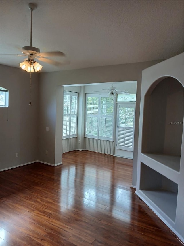 empty room with ceiling fan, plenty of natural light, dark wood-type flooring, and a textured ceiling