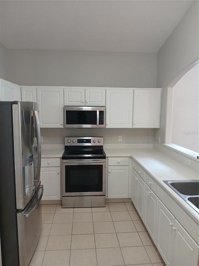 kitchen with light tile patterned floors, stainless steel appliances, white cabinetry, and sink