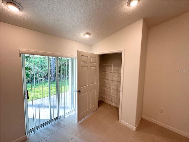 unfurnished room featuring a textured ceiling, vaulted ceiling, and light tile floors