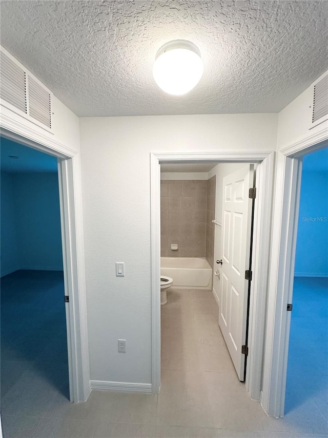 hall with a textured ceiling and tile floors