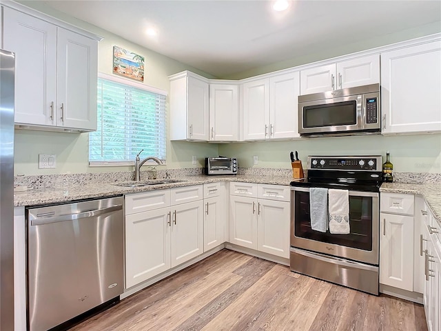 kitchen with stainless steel appliances, sink, white cabinets, and light wood-type flooring