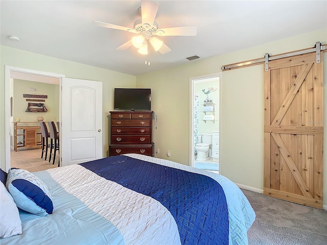 bedroom featuring ceiling fan, ensuite bath, a barn door, and light carpet