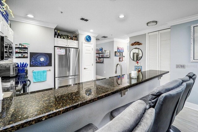 kitchen featuring ornamental molding, stainless steel appliances, light hardwood / wood-style floors, white cabinetry, and a breakfast bar area