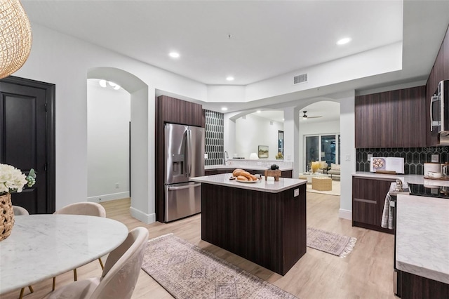 kitchen featuring dark brown cabinets, light hardwood / wood-style flooring, tasteful backsplash, a center island, and stainless steel appliances