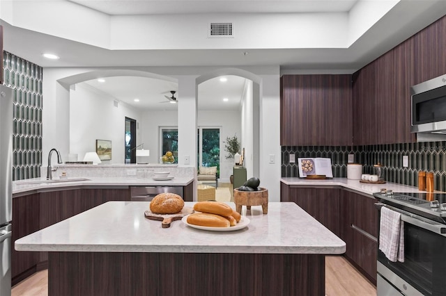 kitchen with stainless steel appliances, a center island, sink, ceiling fan, and dark brown cabinetry