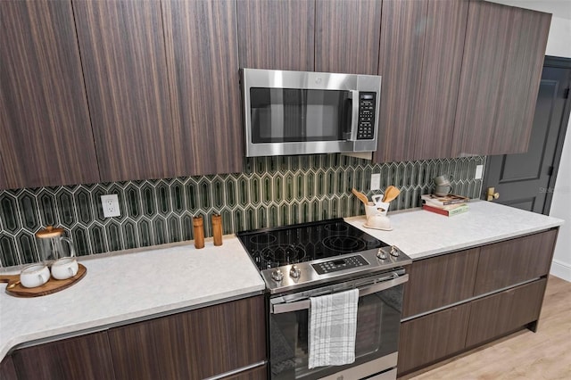 kitchen featuring appliances with stainless steel finishes, dark brown cabinets, decorative backsplash, and light hardwood / wood-style floors