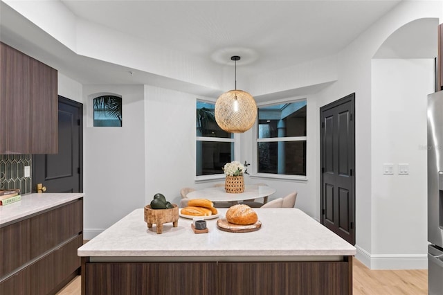 interior space with light wood-type flooring, dark brown cabinets, decorative light fixtures, and a center island