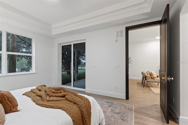 bedroom with light wood-type flooring, a tray ceiling, and ornamental molding