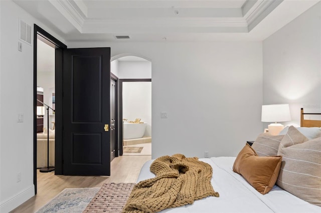 bedroom featuring a tray ceiling, connected bathroom, crown molding, and light hardwood / wood-style flooring