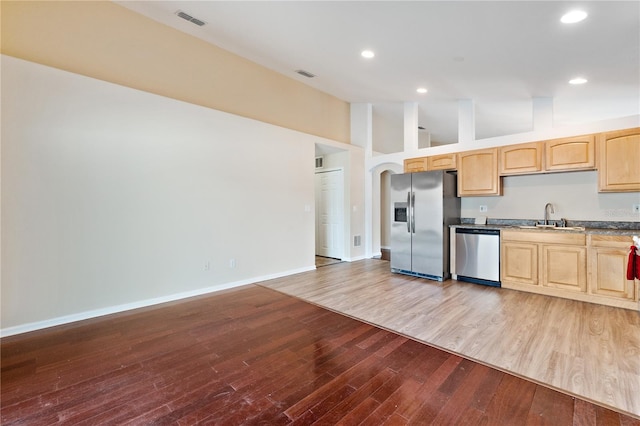 kitchen with high vaulted ceiling, hardwood / wood-style flooring, stainless steel appliances, and light brown cabinetry