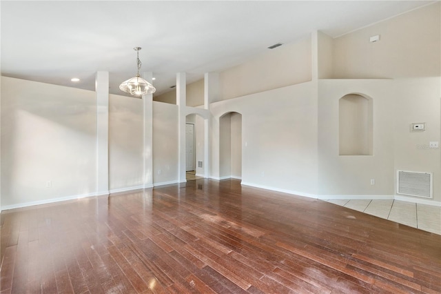 empty room featuring high vaulted ceiling, wood-type flooring, and an inviting chandelier