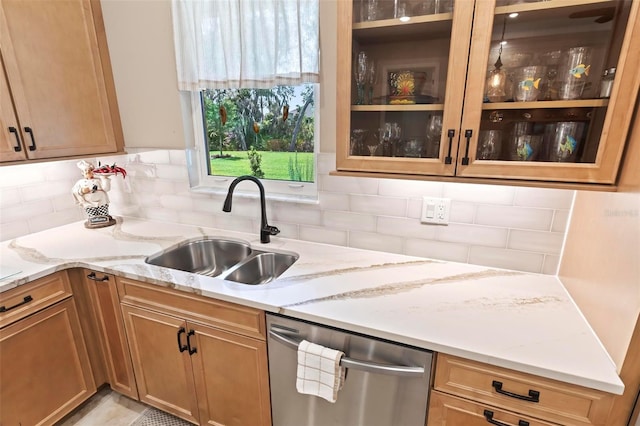 kitchen with light stone counters, stainless steel dishwasher, sink, and decorative backsplash