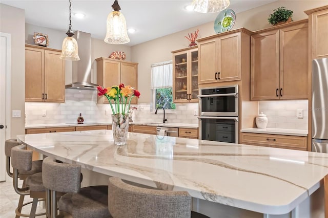 kitchen with pendant lighting, wall chimney range hood, appliances with stainless steel finishes, a kitchen island, and a kitchen bar