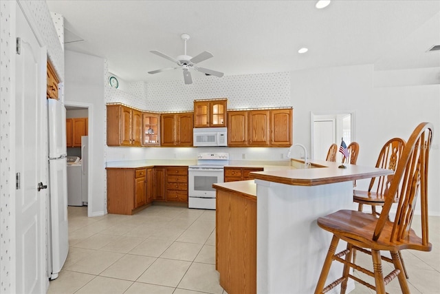 kitchen featuring a kitchen bar, kitchen peninsula, white appliances, ceiling fan, and washer / clothes dryer