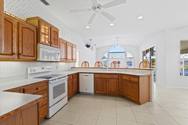 kitchen featuring sink, tasteful backsplash, kitchen peninsula, lofted ceiling, and white appliances