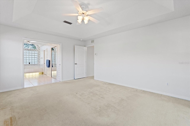 carpeted empty room featuring ceiling fan and a raised ceiling