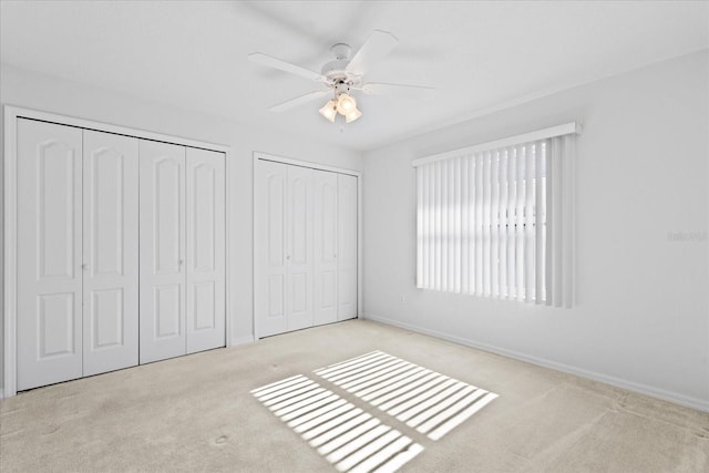 unfurnished bedroom featuring ceiling fan, light carpet, and two closets