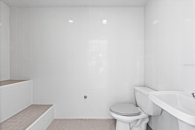 bathroom featuring tile patterned floors, toilet, sink, and tile walls