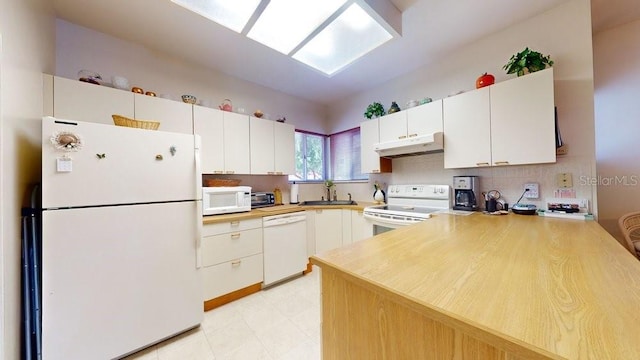 kitchen with kitchen peninsula, white appliances, light tile floors, sink, and white cabinets