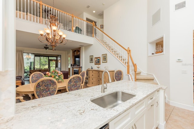 kitchen featuring white cabinets, an inviting chandelier, light stone counters, sink, and light tile floors