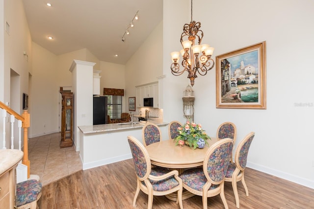 tiled dining area with high vaulted ceiling, sink, a chandelier, and rail lighting