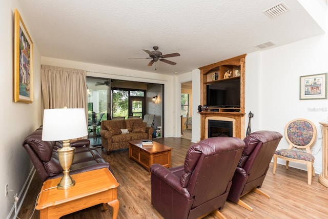 living room with hardwood / wood-style flooring, a large fireplace, a textured ceiling, and ceiling fan