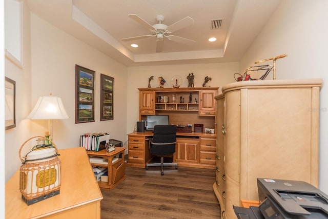 home office with dark wood-type flooring, ceiling fan, and a tray ceiling