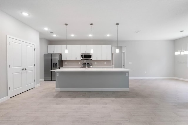 kitchen with backsplash, hanging light fixtures, a center island with sink, white cabinetry, and appliances with stainless steel finishes