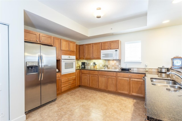 kitchen featuring sink, white appliances, backsplash, and a raised ceiling