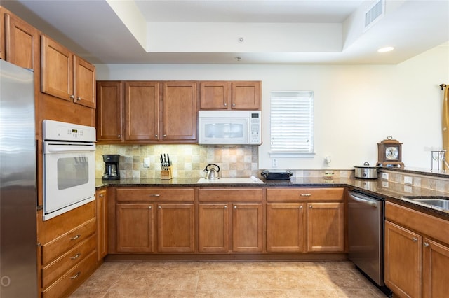 kitchen featuring stainless steel appliances, dark stone countertops, a tray ceiling, and tasteful backsplash