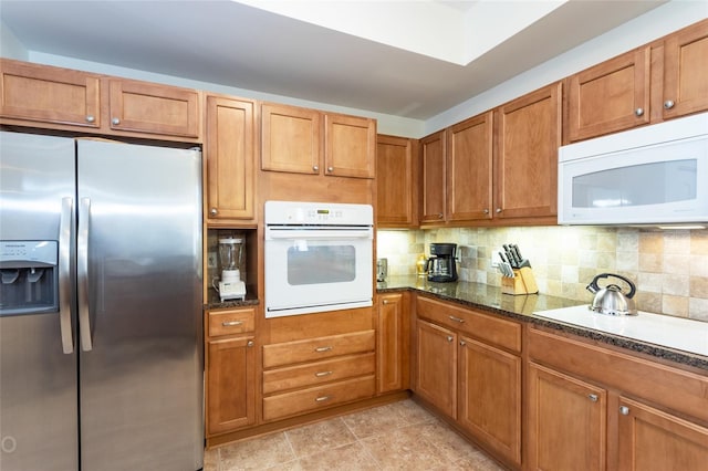 kitchen featuring white appliances, decorative backsplash, and dark stone counters