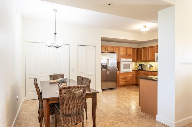 interior space with white appliances, pendant lighting, an inviting chandelier, and backsplash