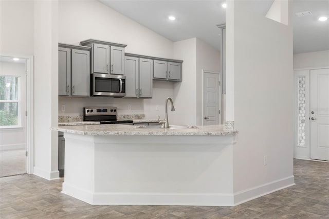 kitchen with sink, gray cabinets, stainless steel appliances, light stone counters, and kitchen peninsula