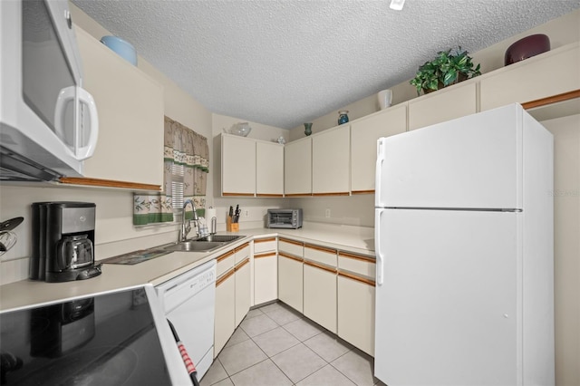 kitchen featuring a textured ceiling, light tile patterned flooring, white appliances, and sink