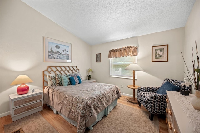 bedroom featuring light wood-type flooring, a textured ceiling, and vaulted ceiling