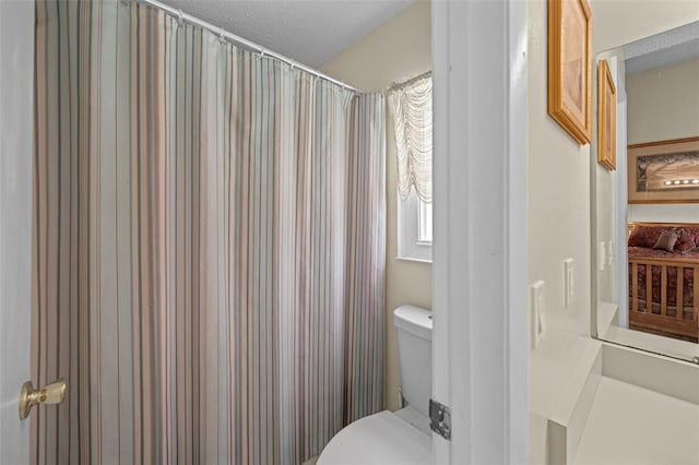 bathroom with a shower with curtain, toilet, and a textured ceiling