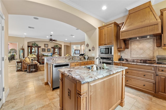 kitchen featuring arched walkways, a kitchen island with sink, custom exhaust hood, stainless steel appliances, and a sink