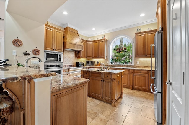 kitchen featuring a center island with sink, custom range hood, a sink, stainless steel appliances, and backsplash