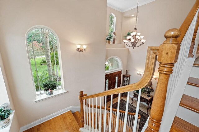 stairway with crown molding, hardwood / wood-style flooring, and a chandelier