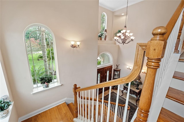 stairway featuring a healthy amount of sunlight, an inviting chandelier, baseboards, and wood finished floors