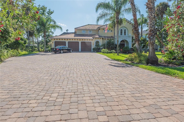 mediterranean / spanish home featuring a garage, decorative driveway, a tiled roof, and stucco siding