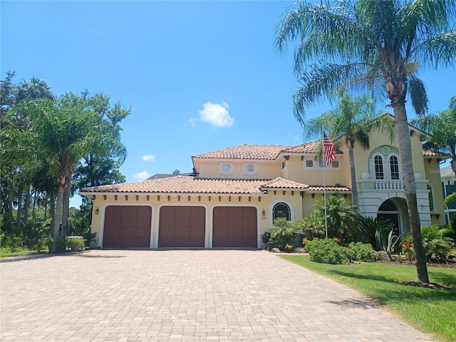 mediterranean / spanish home featuring a garage, a tiled roof, decorative driveway, and stucco siding