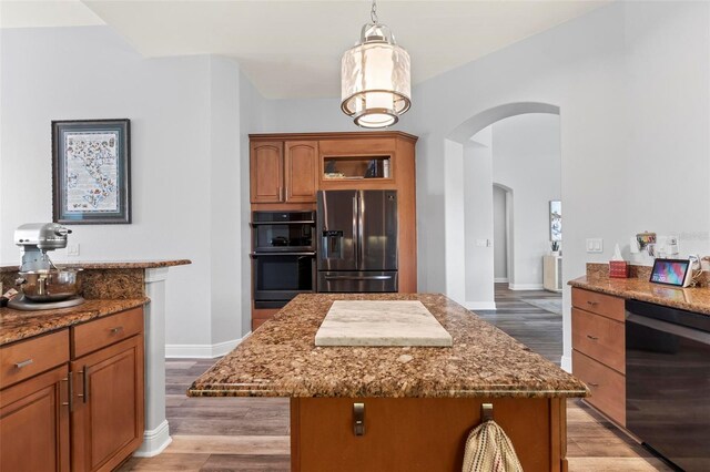 kitchen featuring light wood-type flooring, black appliances, a kitchen island, and decorative light fixtures