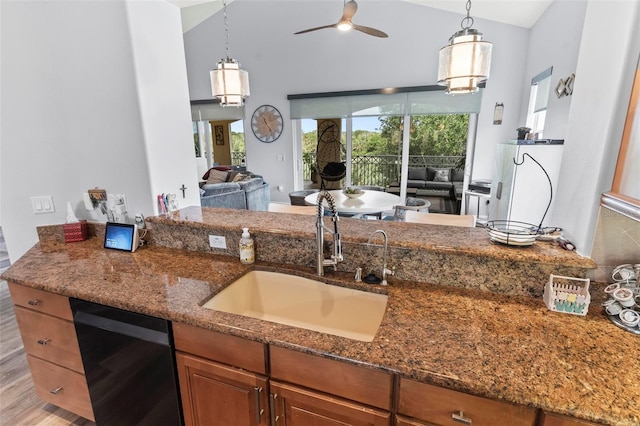 kitchen with hanging light fixtures, black dishwasher, sink, vaulted ceiling, and dark stone counters